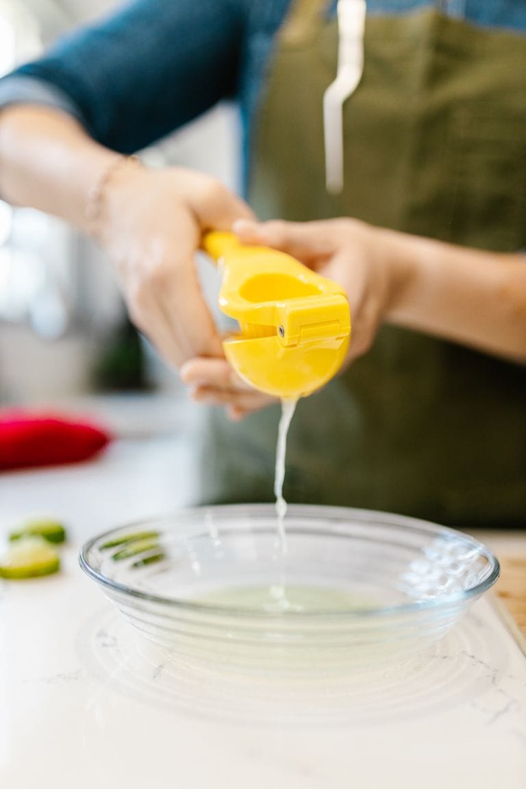 Close-up of hands squeezing fresh lime juice into a clear bowl for cooking purposes.
